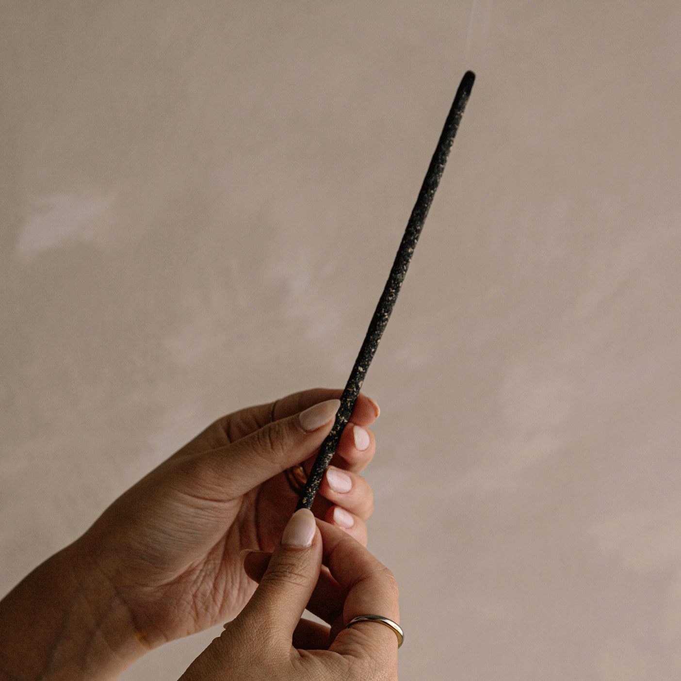 Hand holding smoldering incense stick with gentle smoke rising